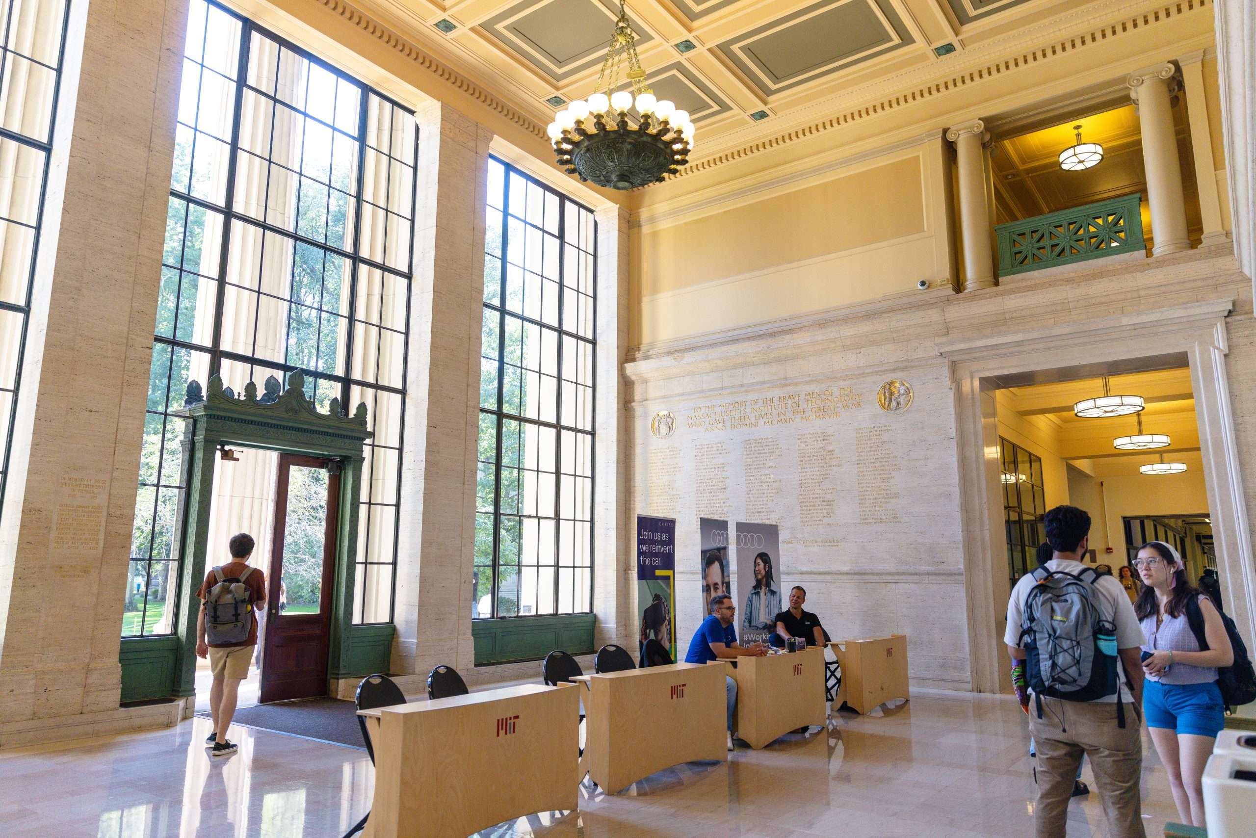 Students gather inside an MIT building with floor to ceiling windows.