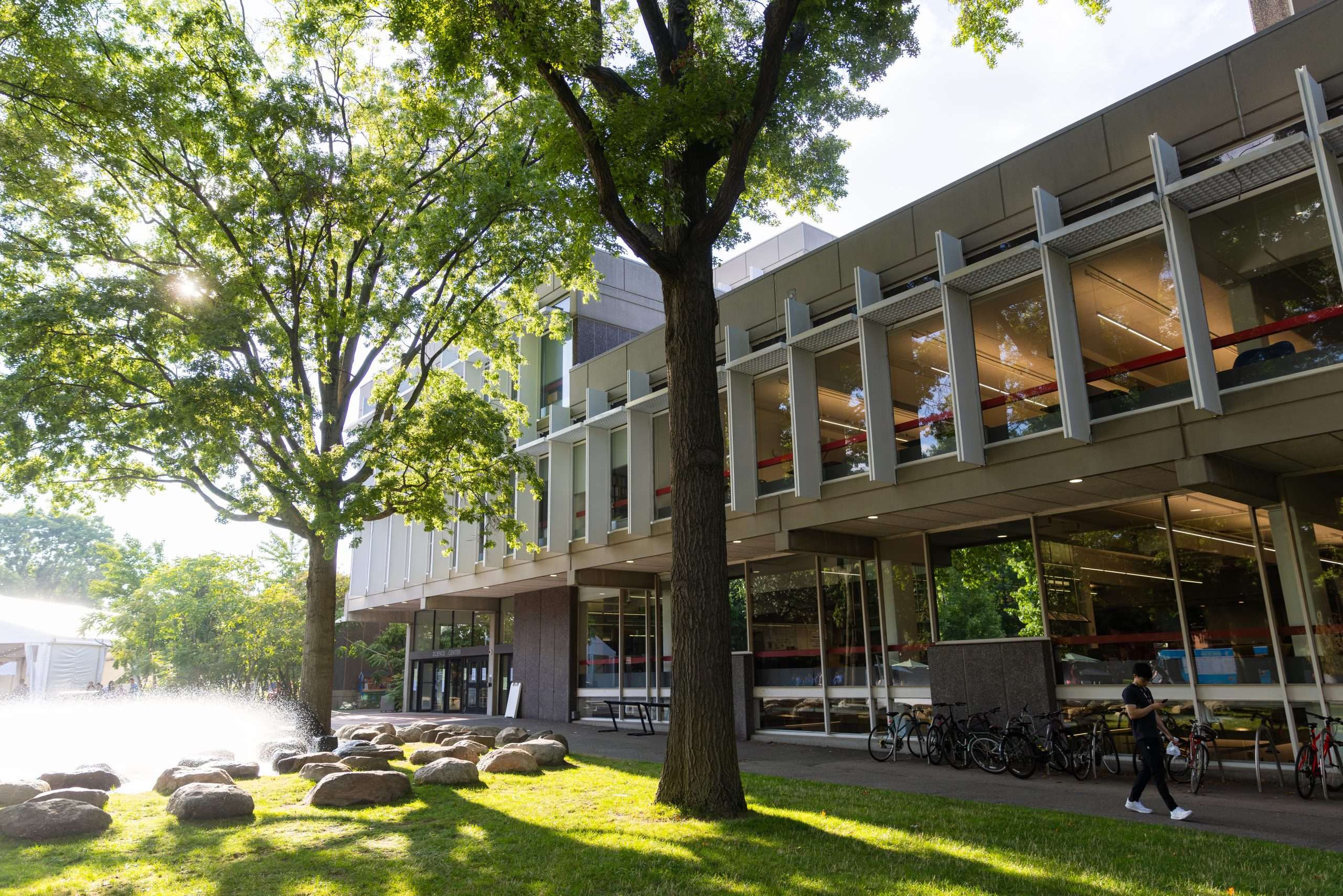 A student walks by a fountain outside a glass building at Harvard University.