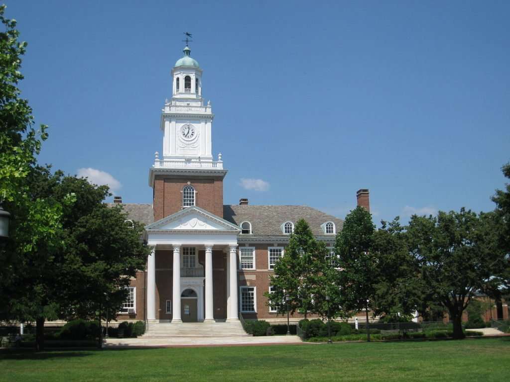 A lawn is featured in front of a brick building with white columns at Johns Hopkins University.