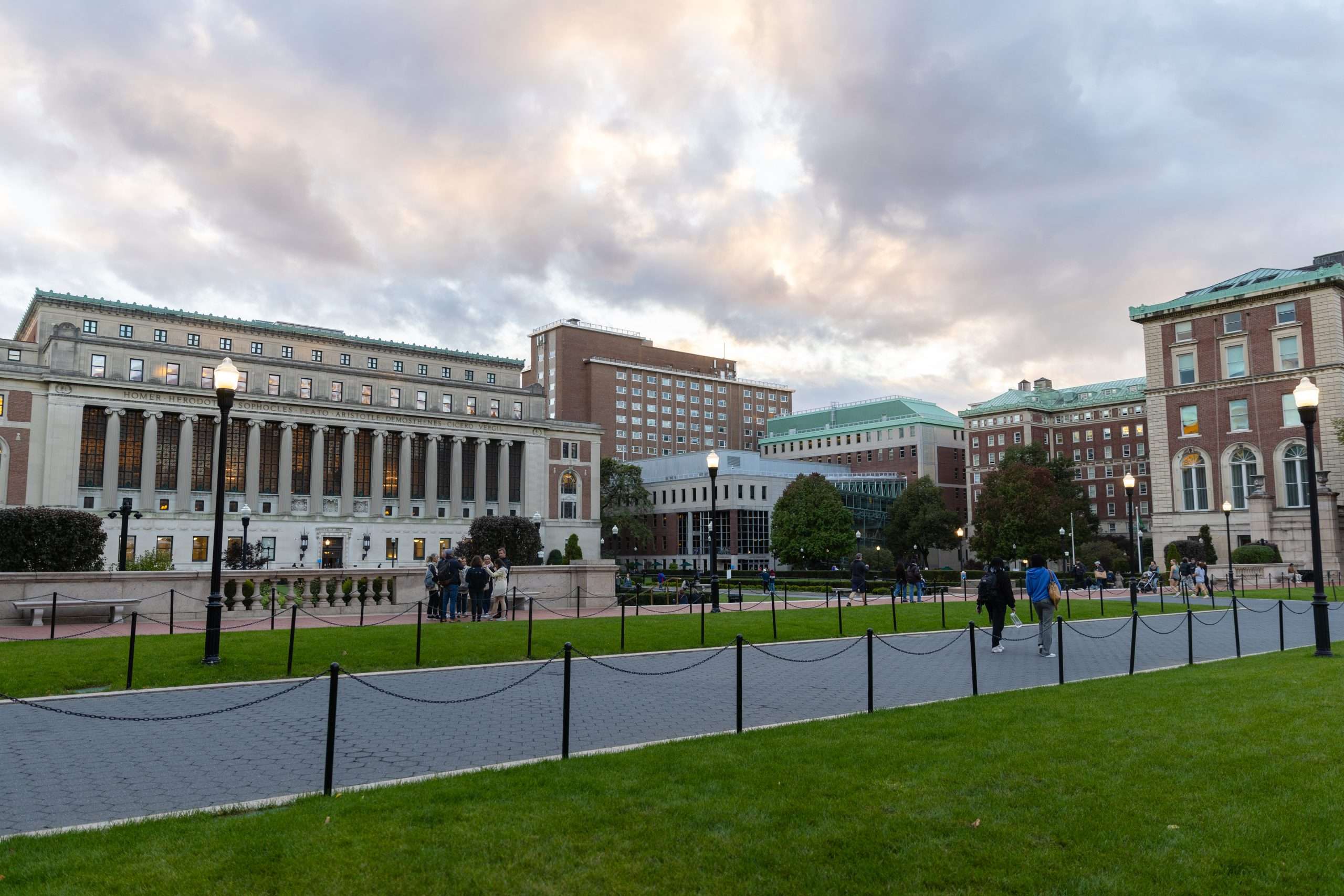 Students walk across Columbia's quad under a cloudy sky.