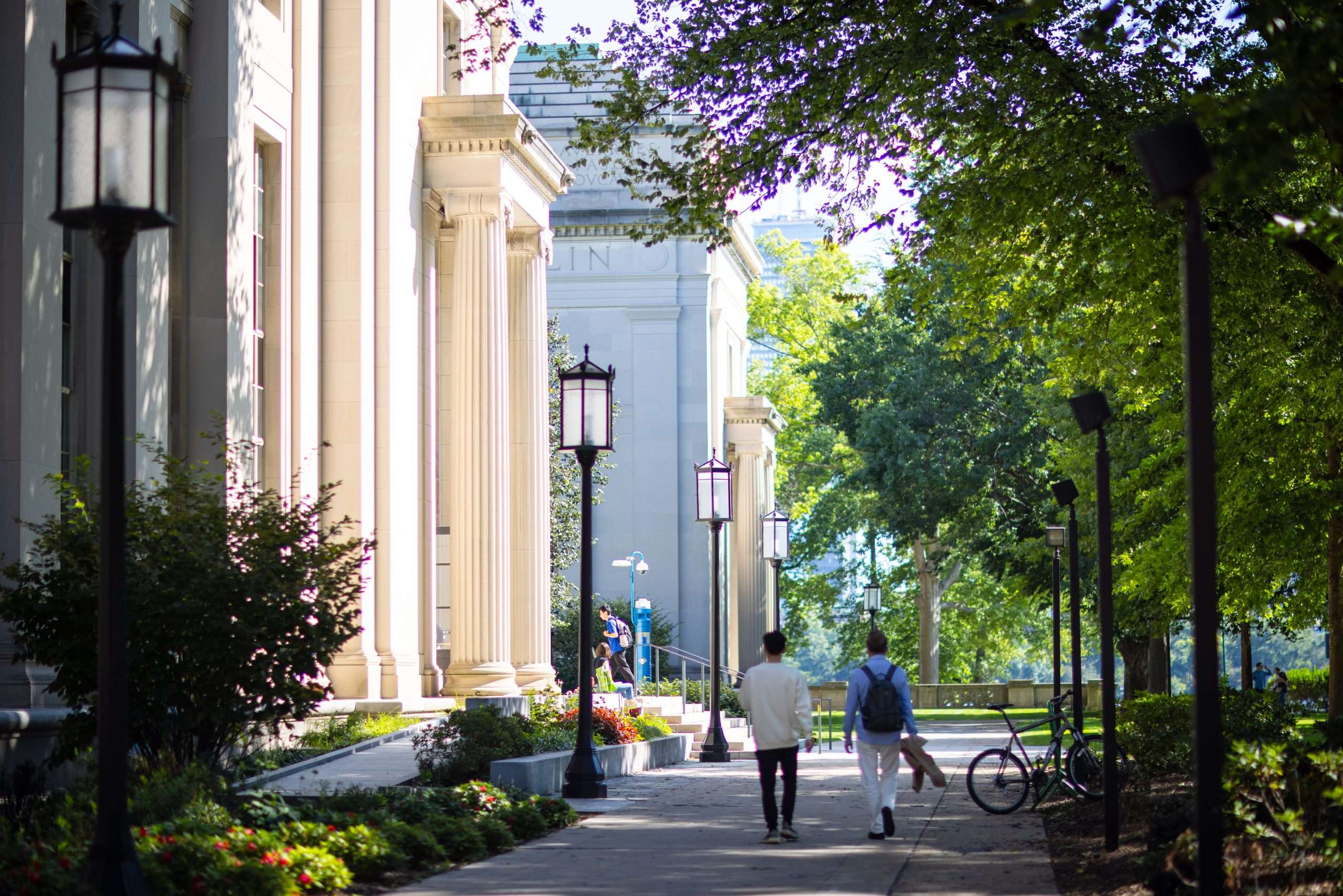 Students walk in front of a white columned building at MIT.