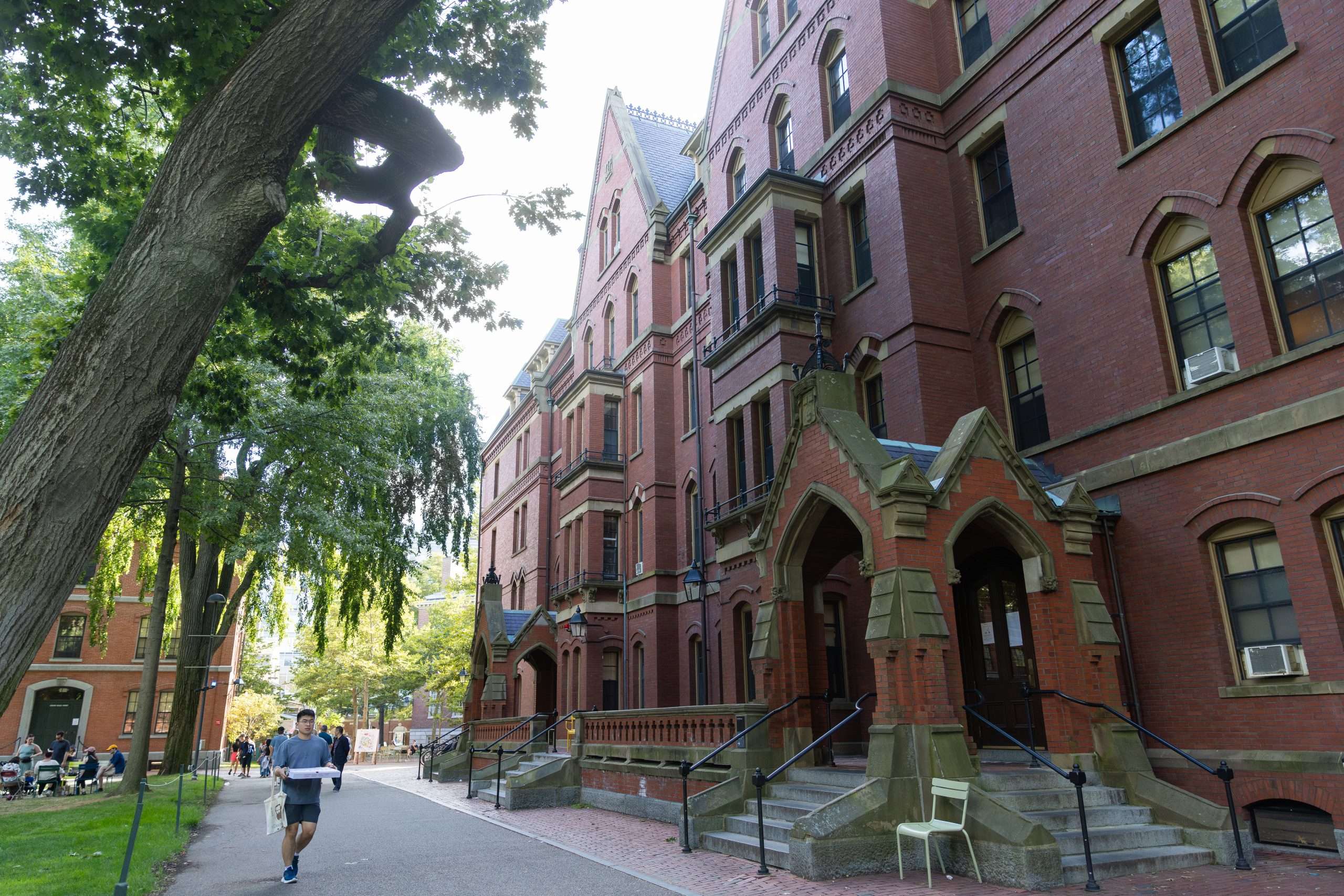 A man carries a pizza box in front of a castle-like building at Harvard University.