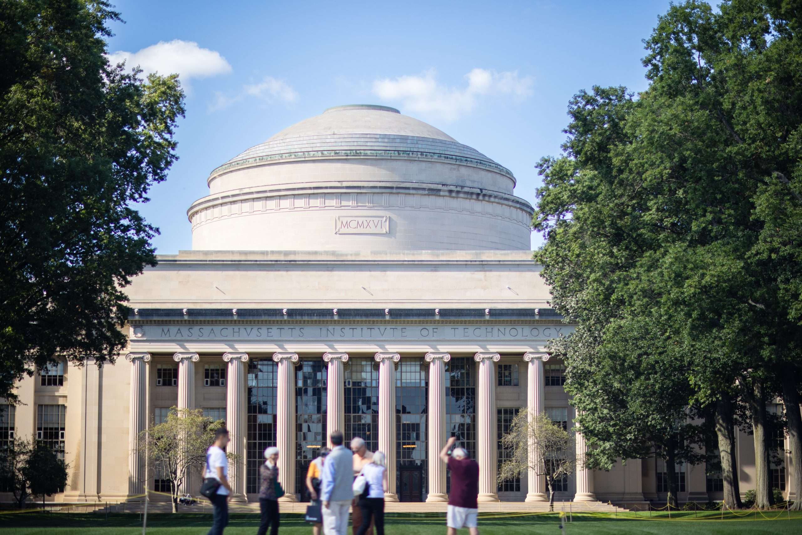 People stand in front of a dome-like building with columns at the Massachusetts Institute of Technology.