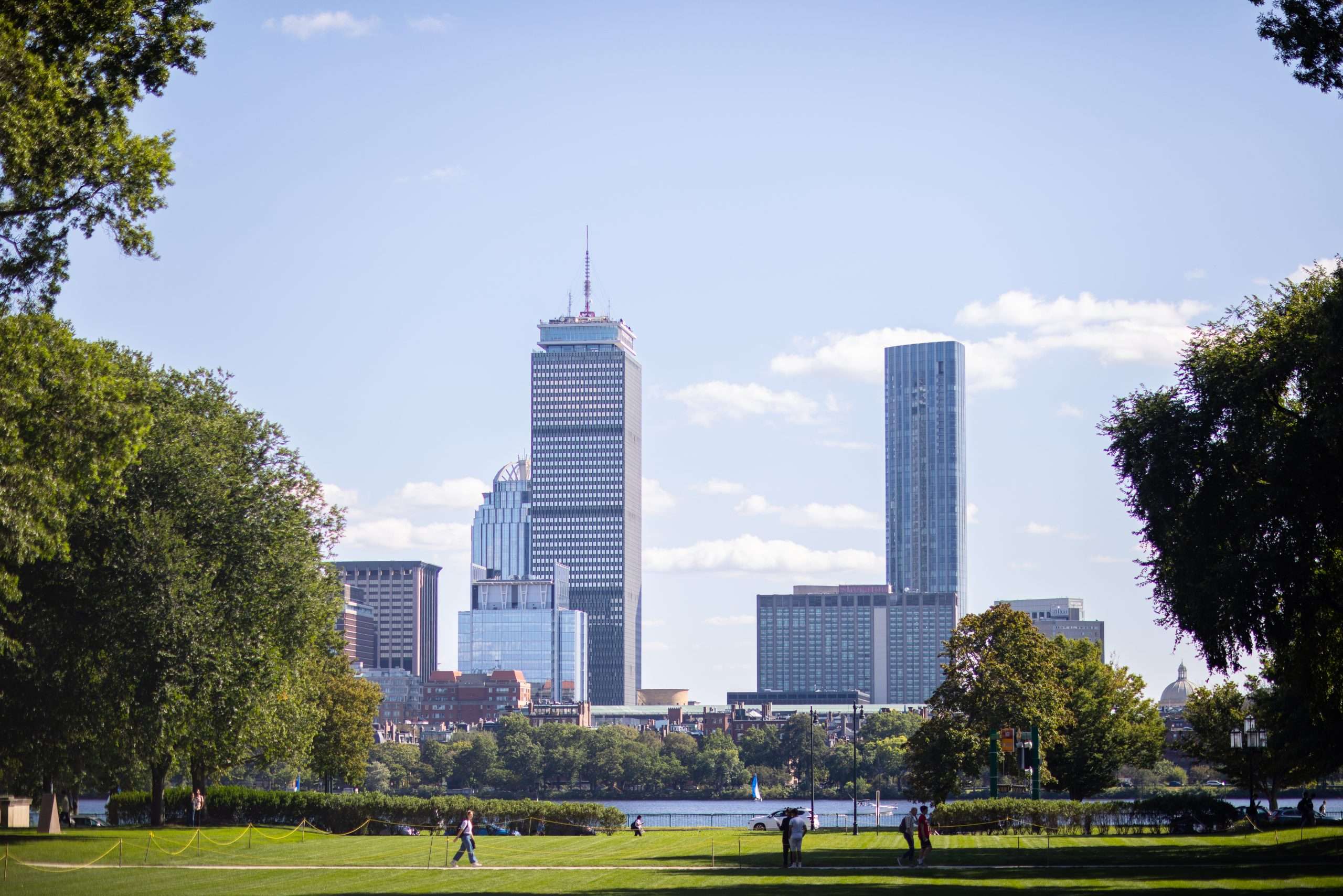 Students walk on a lawn on MIT's campus, with The Charles River in the background.